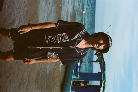 Sideways image of male model with longer hair and a mustache wearing the full 'Agua Magica' Cabana Set while standing ankle deep in the ocean.