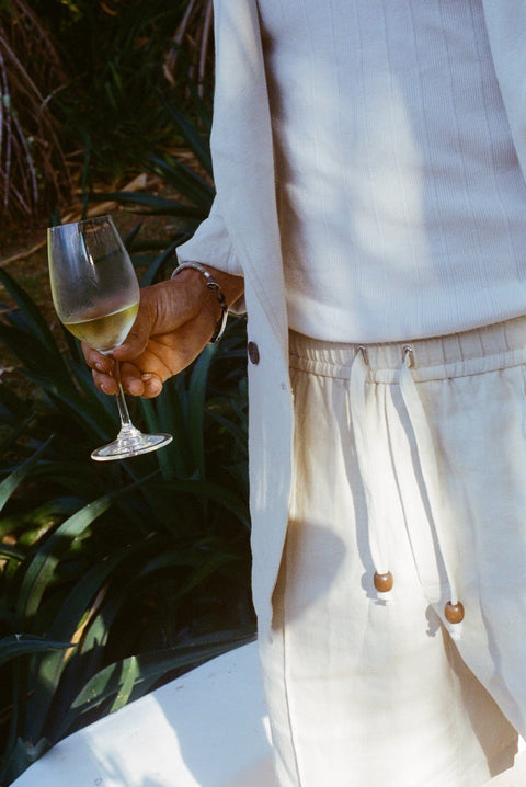 Close-up of man wearing the sand linen shorts while holding a glass of white wine.
