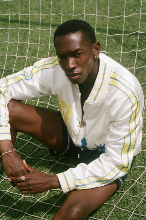 Person wearing a white FIFA souvenir jacket with yellow accents on a grassy field.