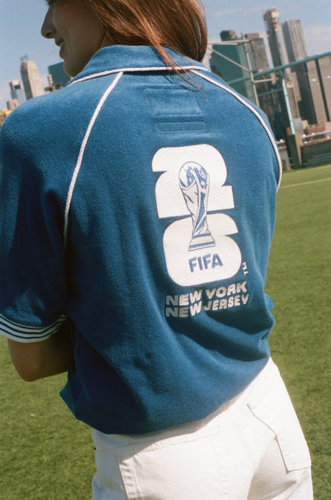 Back view of a blue terry quarter-zip polo with a large FIFA New York New Jersey graphic and World Cup trophy motif.