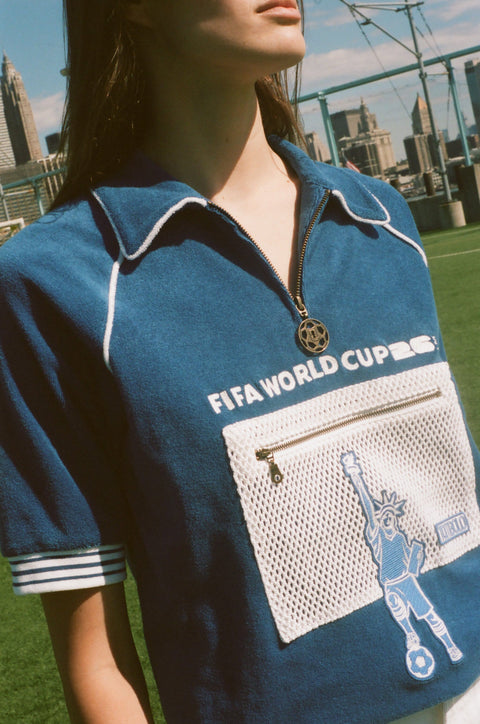 Close-up of a blue terry quarter-zip polo with FIFA World Cup 26 embroidery, a mesh zip pocket, and a Statue of Liberty graphic.
