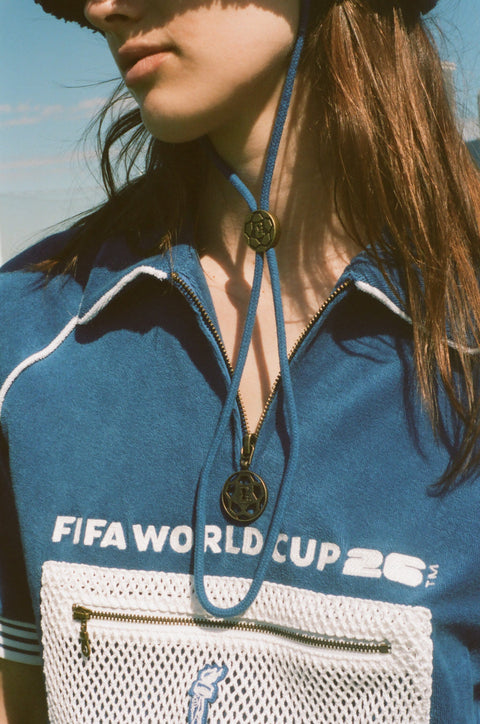 Close-up of a blue terry quarter-zip polo with FIFA World Cup 26 embroidery, a mesh zip pocket, and soccer ball cord stoppers.