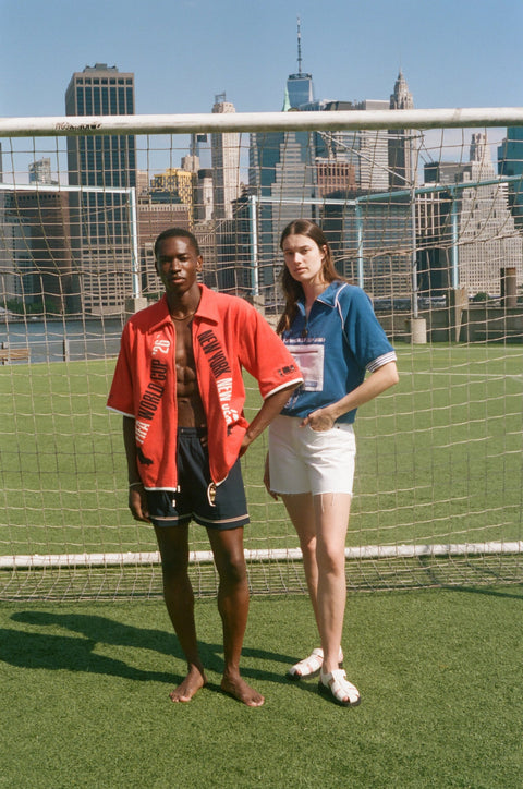 Two models wearing FIFA collection tops stand in front of a soccer goal net with the New York City skyline behind them.