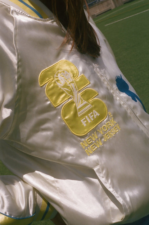 Close-up of a white jacket with FIFA logo and 'New York New Jersey' text on a grassy field.