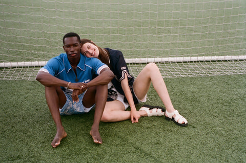 Two people sitting on a grassy field with a soccer goal in the background