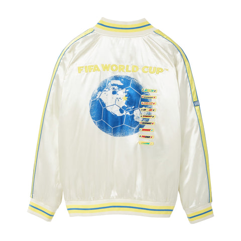 Back of a white satin bomber jacket with yellow and blue striped trim, yellow “FIFA World Cup™” embroidery, a large blue globe and soccer ball graphic, colorful embroidered destination tags, and striped shoulder details.