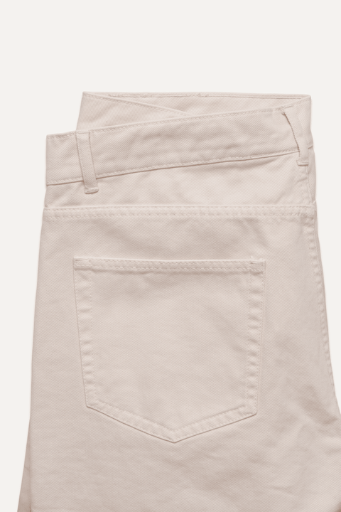 Close-up of the back waistband and pocket area of cream jean, showing belt loops, stitching, and a single back pocket on a plain light background - Inkerman NYC