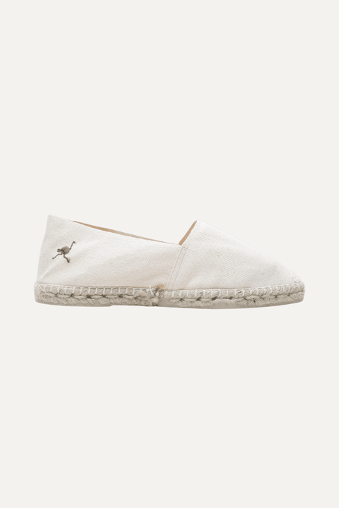 A single cream canvas espadrille slip-on shoe with a braided jute sole and a small green flamingo logo on the side, shown against a light off-white background - Inkerman NYC