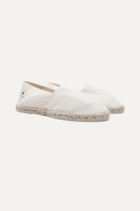 A pair of cream canvas espadrille slip-on shoes with a braided jute sole and a small green flamingo logo on the side, shown against a light off-white background - Inkerman NYC