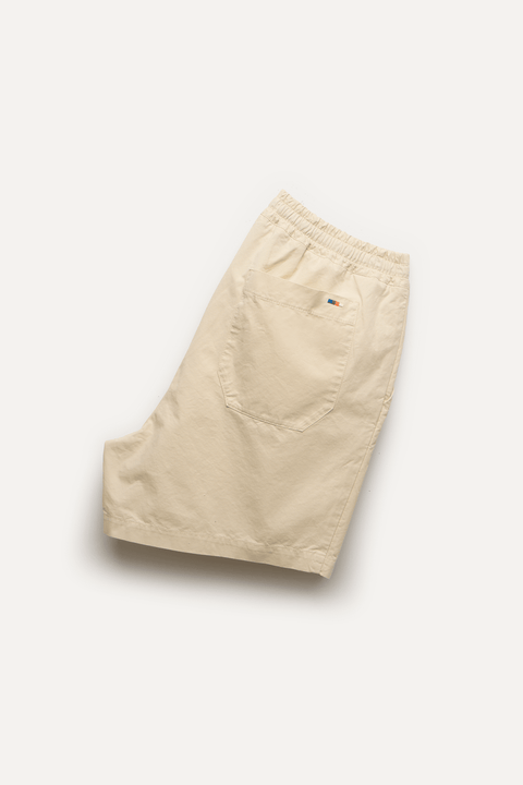 A pair of light beige shorts with an elastic waistband and a back pocket, shown from a top-down view on a white background - Inkerman NYC