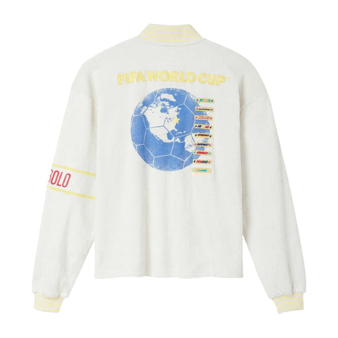 Back view of cream long-sleeve quarter-zip shirt with yellow “FIFA World Cup” lettering and large blue globe graphic with team list on the back, plus striped yellow ribbed collar and cuffs.
