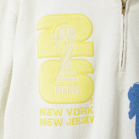 Close-up of yellow embroidered FIFA New York New Jersey graphics on a cream terry quarter-zip pullover.