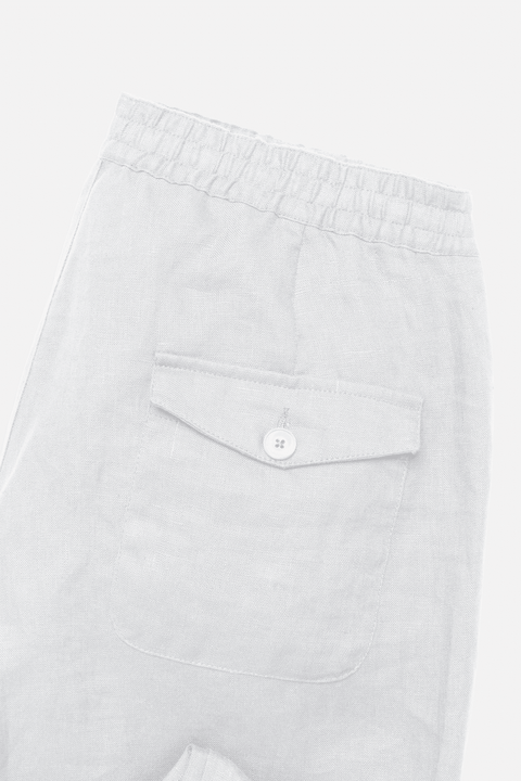 Close-up of white linen trousers showing an elastic waistband and a front flap pocket with a small button closure - Inkerman NYC