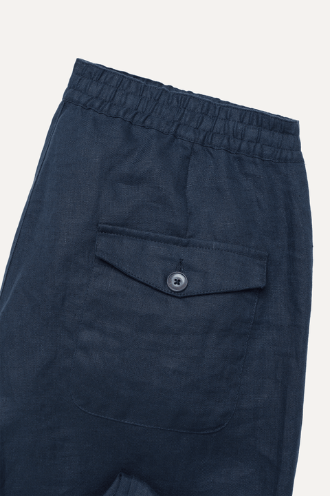 Close-up of navy linen trousers showing the elastic waistband and a front flap pocket with a single button closure - Inkerman NYC