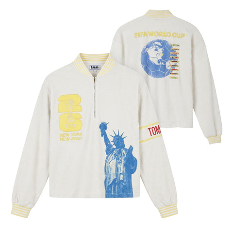 Front and back view of a cream terry long-sleeve quarter-zip featuring striped rib-knit collar and cuffs, embroidered FIFA World Cup 26 New York/New Jersey crest, oversized Statue of Liberty graphic, Tombolo sleeve detail, and a back graphic of a globe-shaped soccer ball.